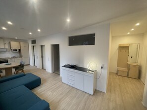 A modern, well-lit room with a kitchenette, a vanity with a mirror, and a seating area with blue sofas. - Modern Apartment in Downtown (Willingen (Upland))