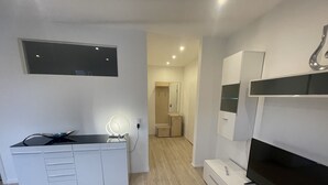 Une pièce moderne et bien éclairée, dotée d’une kitchenette, d’un téléviseur à écran plat et d’un miroir au-dessus du comptoir.