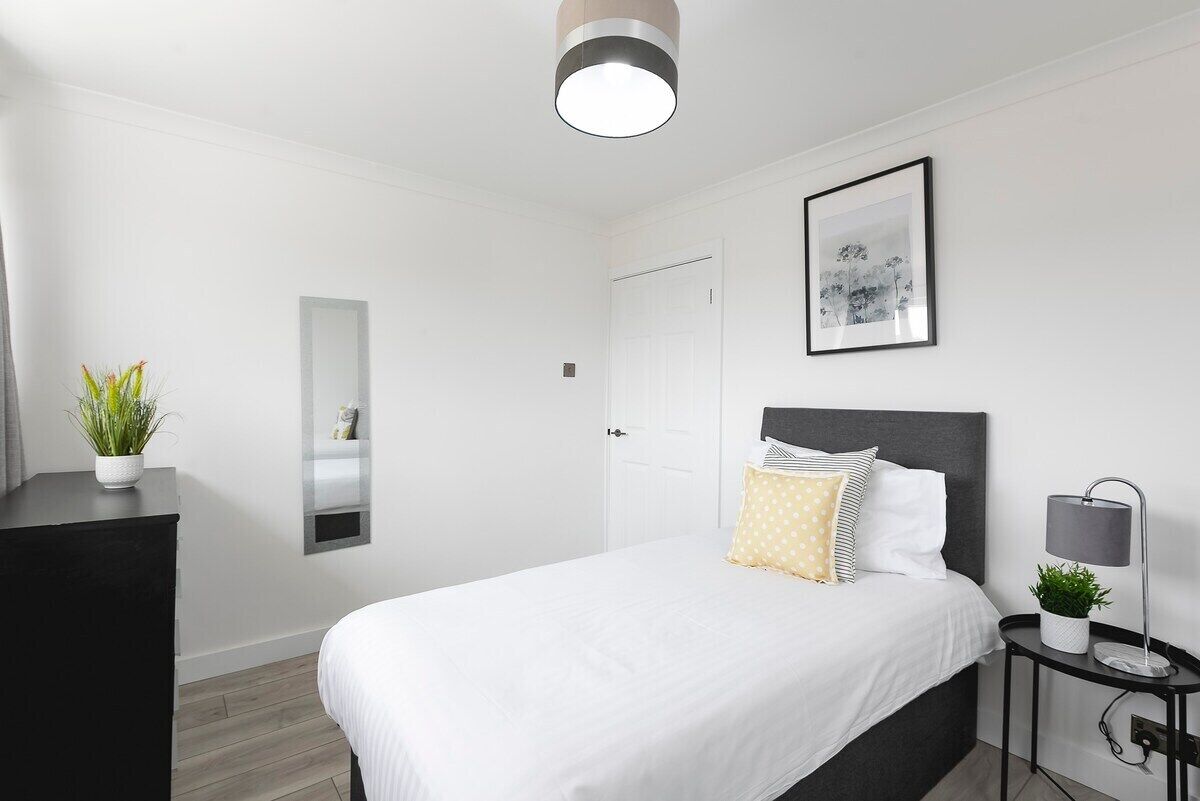 A modern bedroom with a bed, bedside table, lamp, and a framed picture on the wall.