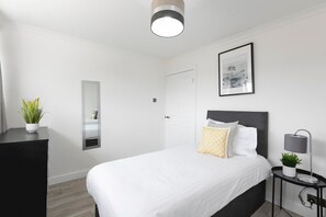 Ein modernes Schlafzimmer mit Bett, Nachttisch, Lampe und einem gerahmten Bild an der Wand.