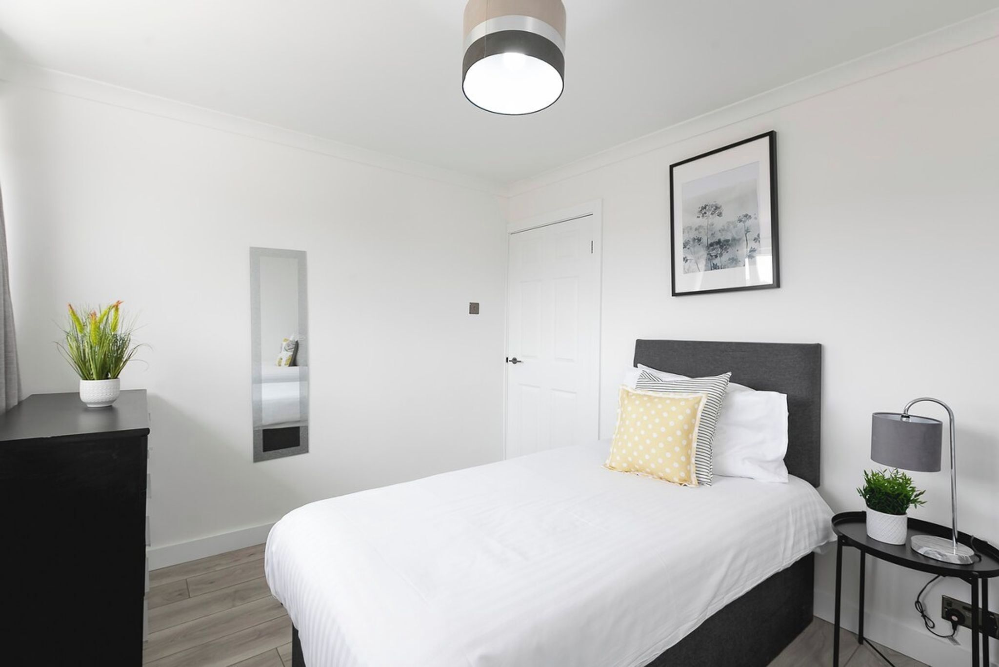 A modern bedroom with a bed, bedside table, lamp, and a framed picture on the wall.