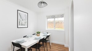 Zona pranzo con tavolo bianco apparecchiata per quattro persone, sedie nere, lampadario singolo e un quadro appeso al muro.