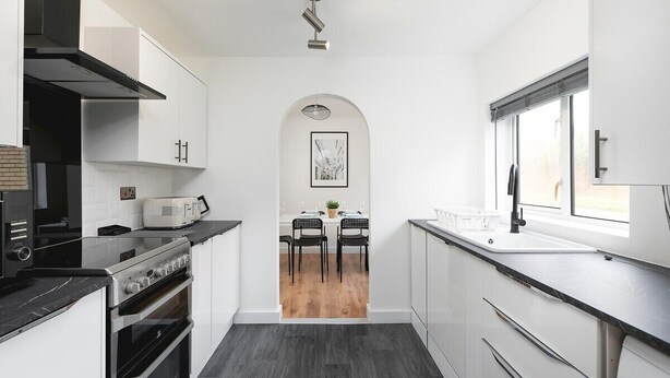 Una cucina moderna con mobili bianchi, un piano di lavoro nero, un forno a incasso, un microonde e una finestra con vista.