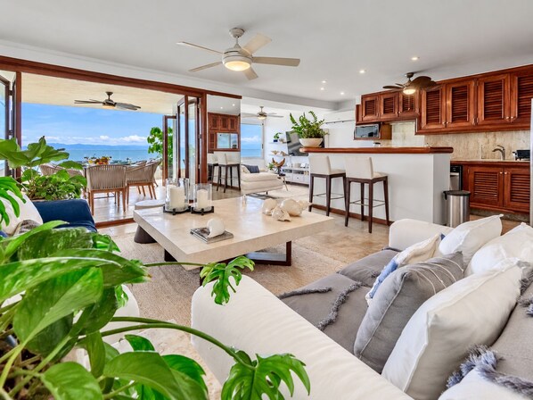 A spacious living area with a view of the ocean, a dining area with a table set for two, and a kitchen with wooden cabinets.