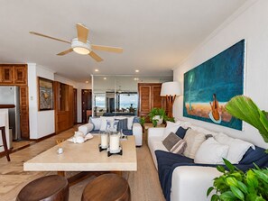 A modern living room with a ceiling fan, a large painting, and a view of the ocean.
