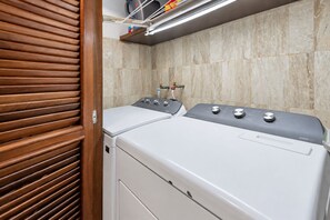 A laundry room with two front-loading washing machines, a wooden slatted door, and a tiled wall. - Private Beach Front with a Spectacular View (Puerto Vallarta)