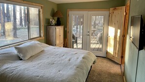 A bedroom with a bed, a cabinet, a door leading to an outdoor patio, and a television. - Cute, cozy, updated cabin in the pines (Pinetop)