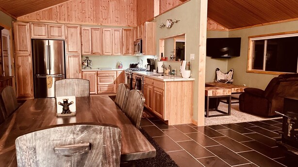 A spacious kitchen with wooden cabinets, a stainless steel refrigerator, and a dining area with a wooden table and chairs. - Cute, cozy, updated cabin in the pines (Pinetop)