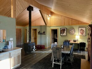 A spacious living area with a high ceiling, a fireplace, a dining table with chairs, and a kitchen area with cabinets and a sink.