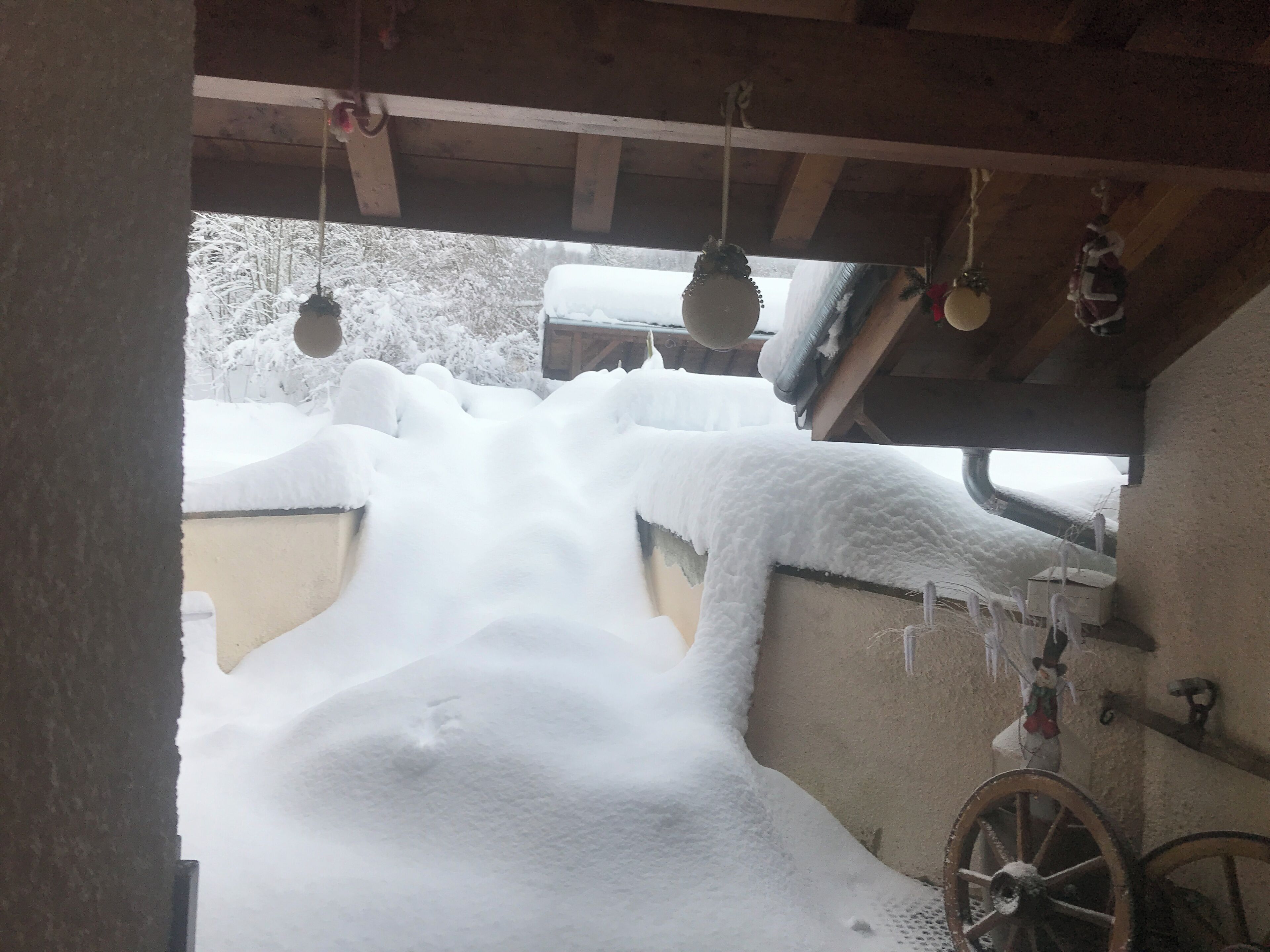 Area esterna innevata con una struttura in legno, una carriola e oggetti appesi.