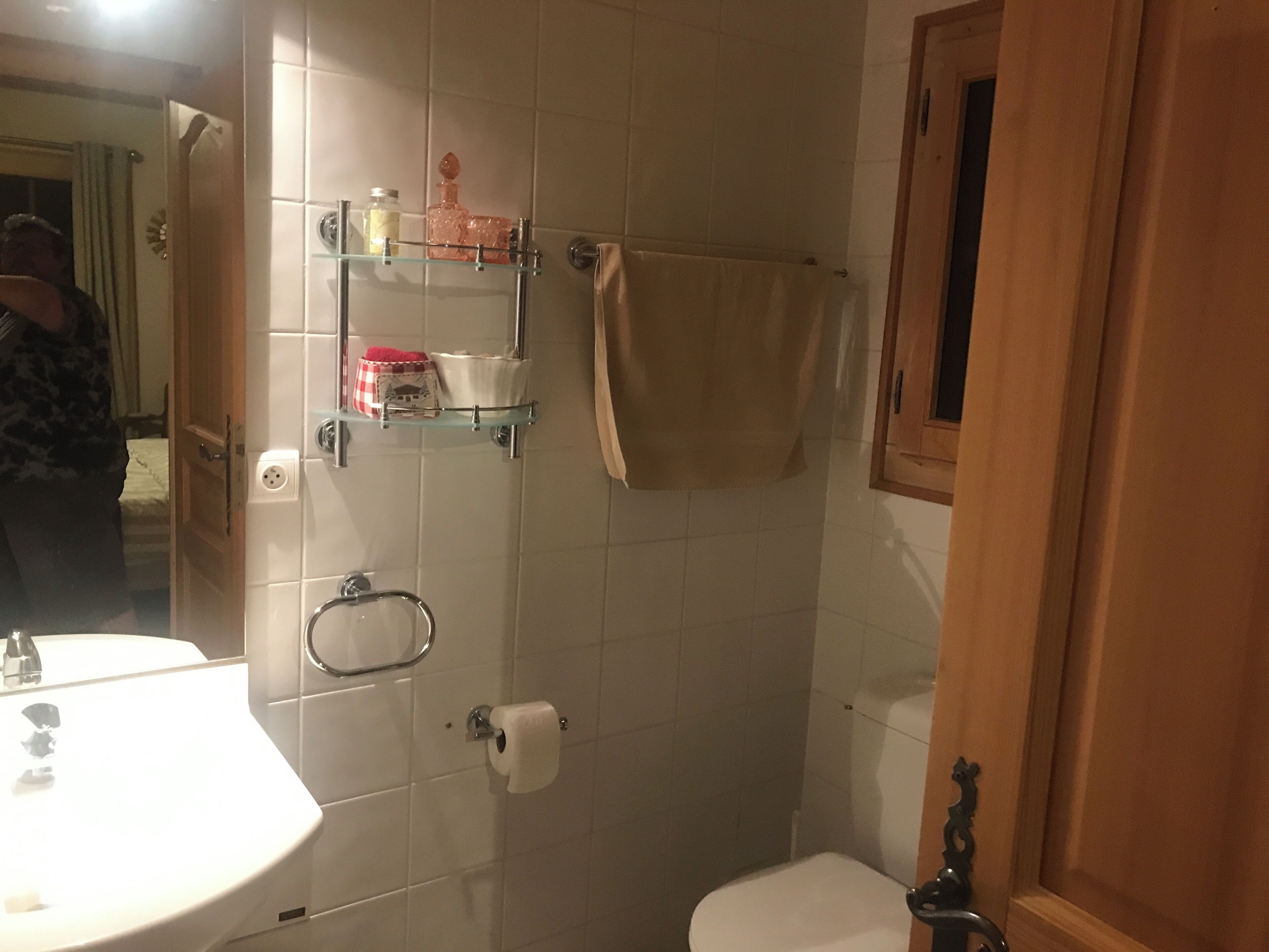 A bathroom with a white sink, toilet, and glass shelves with toiletries.