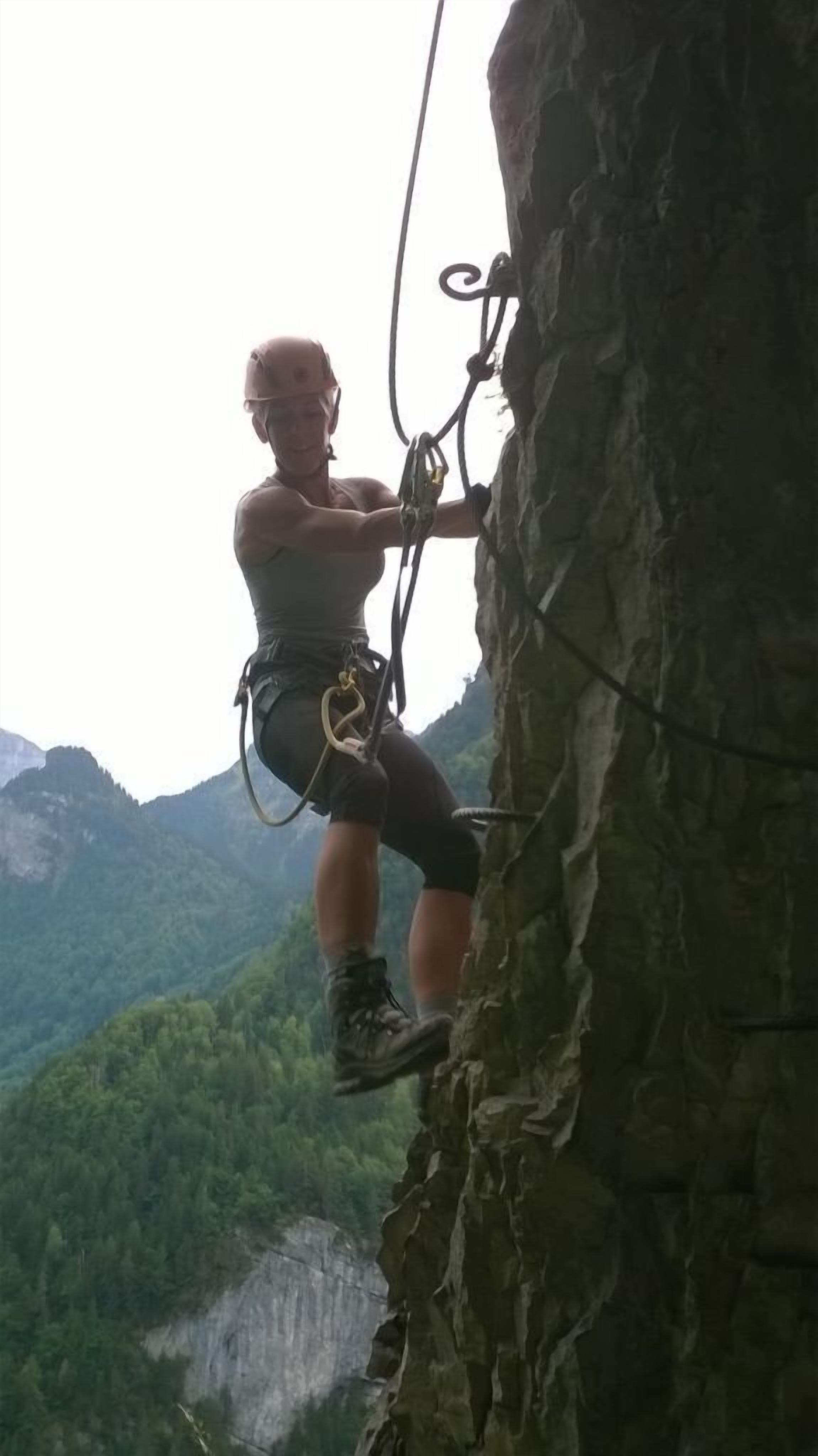 A person rock climbing a cliff with a harness and ropes.