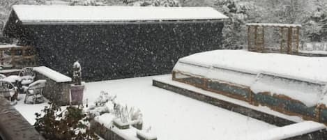A snowy outdoor area with steps leading up to a building, surrounded by trees and a house in the background.