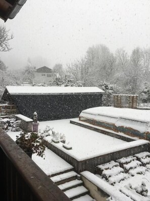 A snowy outdoor area with steps leading up to a building, surrounded by trees and a house in the background.