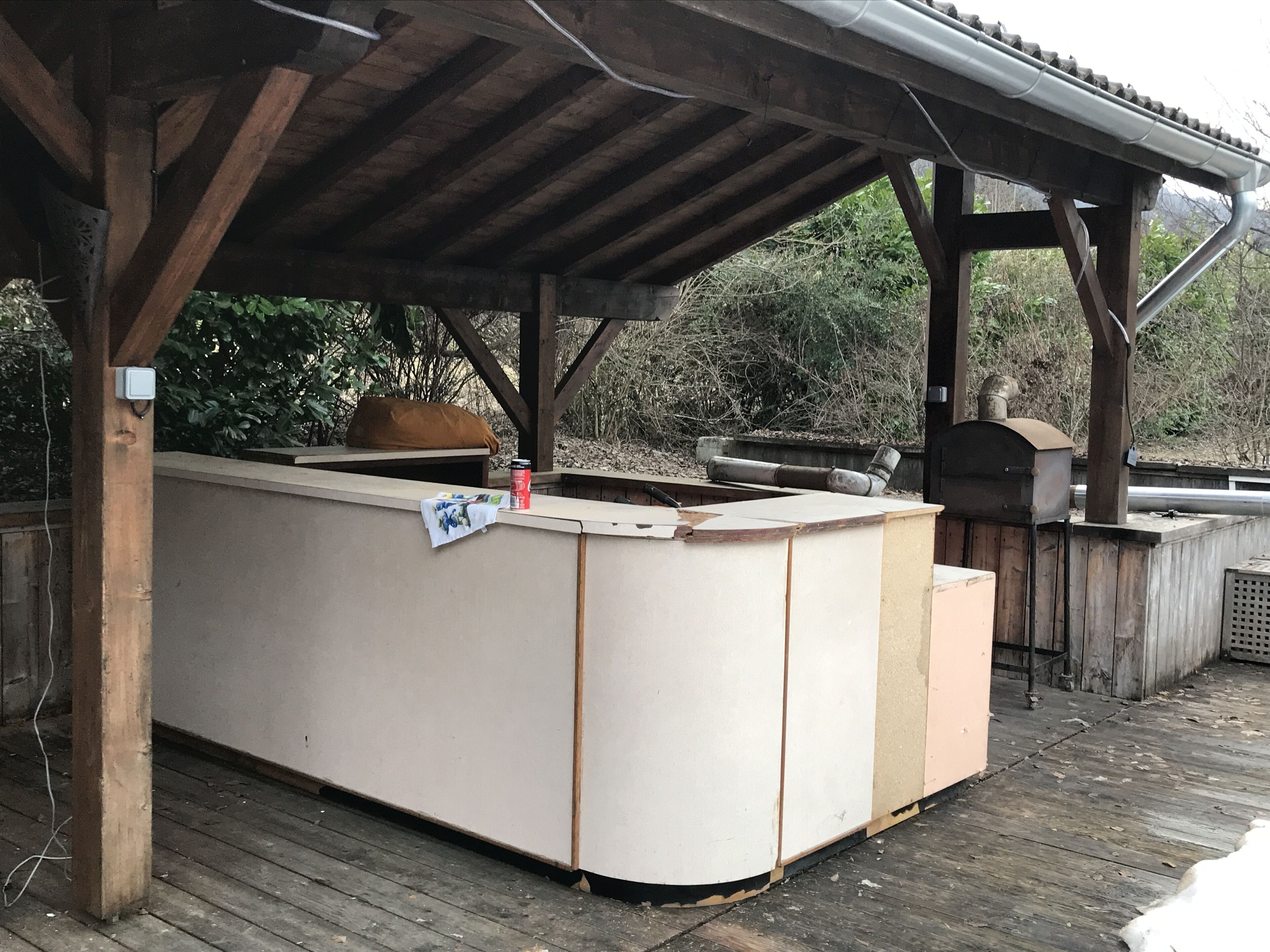 Une terrasse en bois dotée d’un bar intégré, d’un barbecue et d’un espace salon abrité.