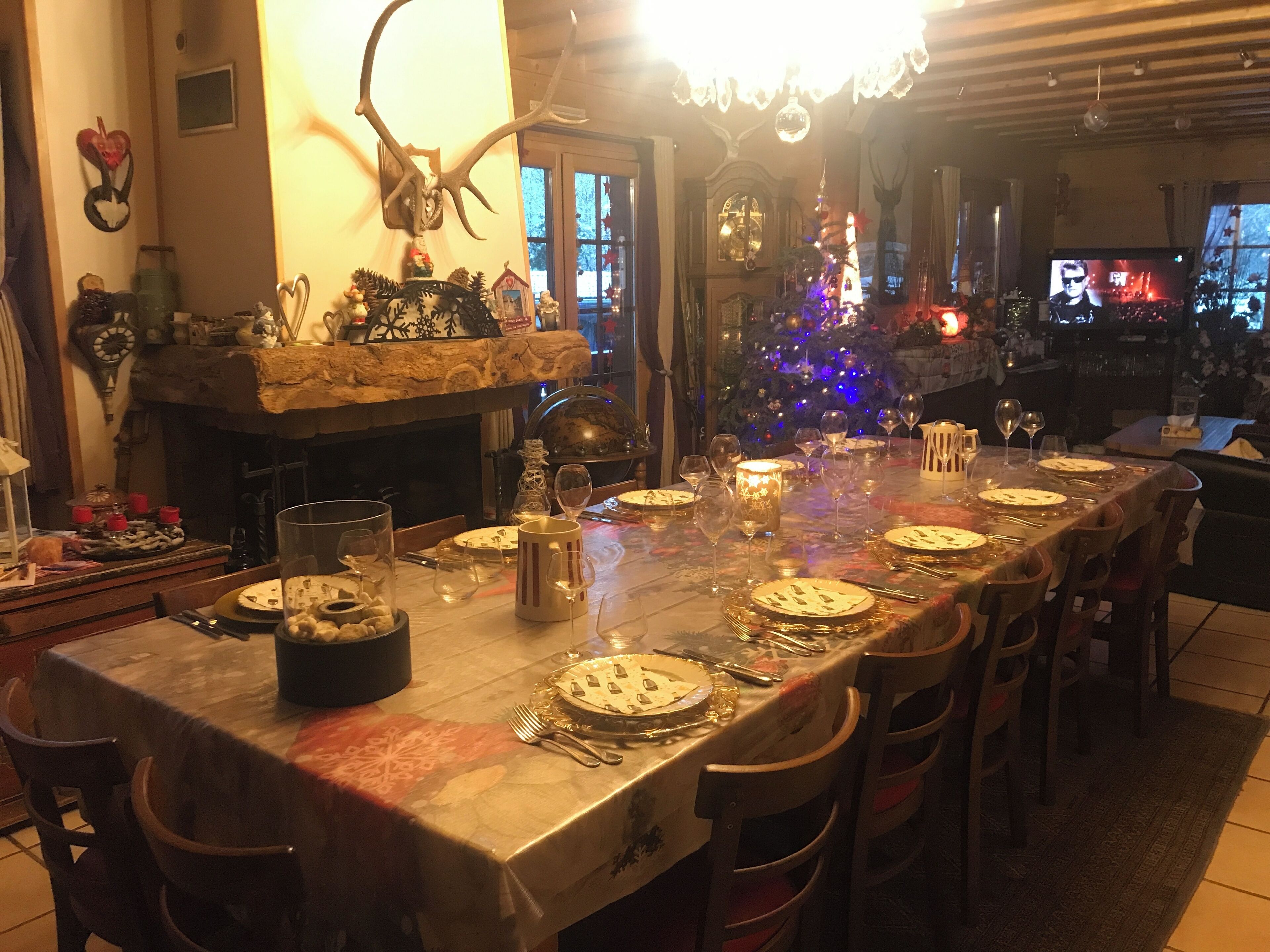 Zona pranzo con un lungo tavolo apparecchiato per un pasto, un camino e un albero di Natale sullo sfondo.