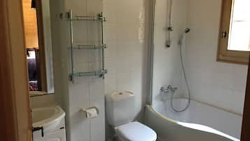 A bathroom with a toilet, a glass shelf, a shower, and a sink.