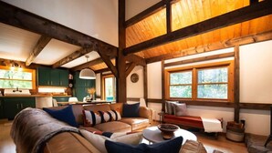 A cozy living room with a sectional sofa, a coffee table, and a fireplace. There is a kitchen area with green cabinets and a window overlooking the outdoors. - Stonebridge Cabin: Modern Amenities, Enjoy Nature! (Lee)