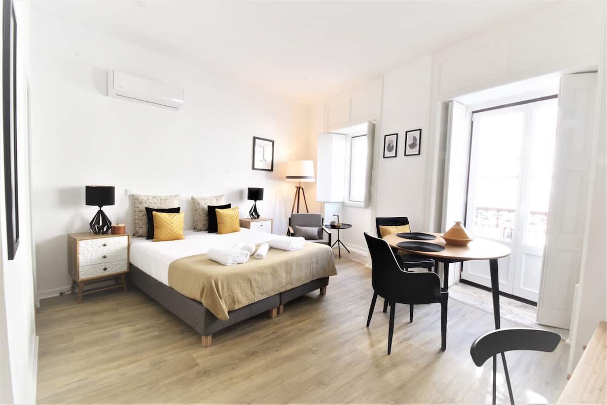 Quarto de hotel moderno com cama, mesas de cabeceira, escrivaninha e cadeiras.