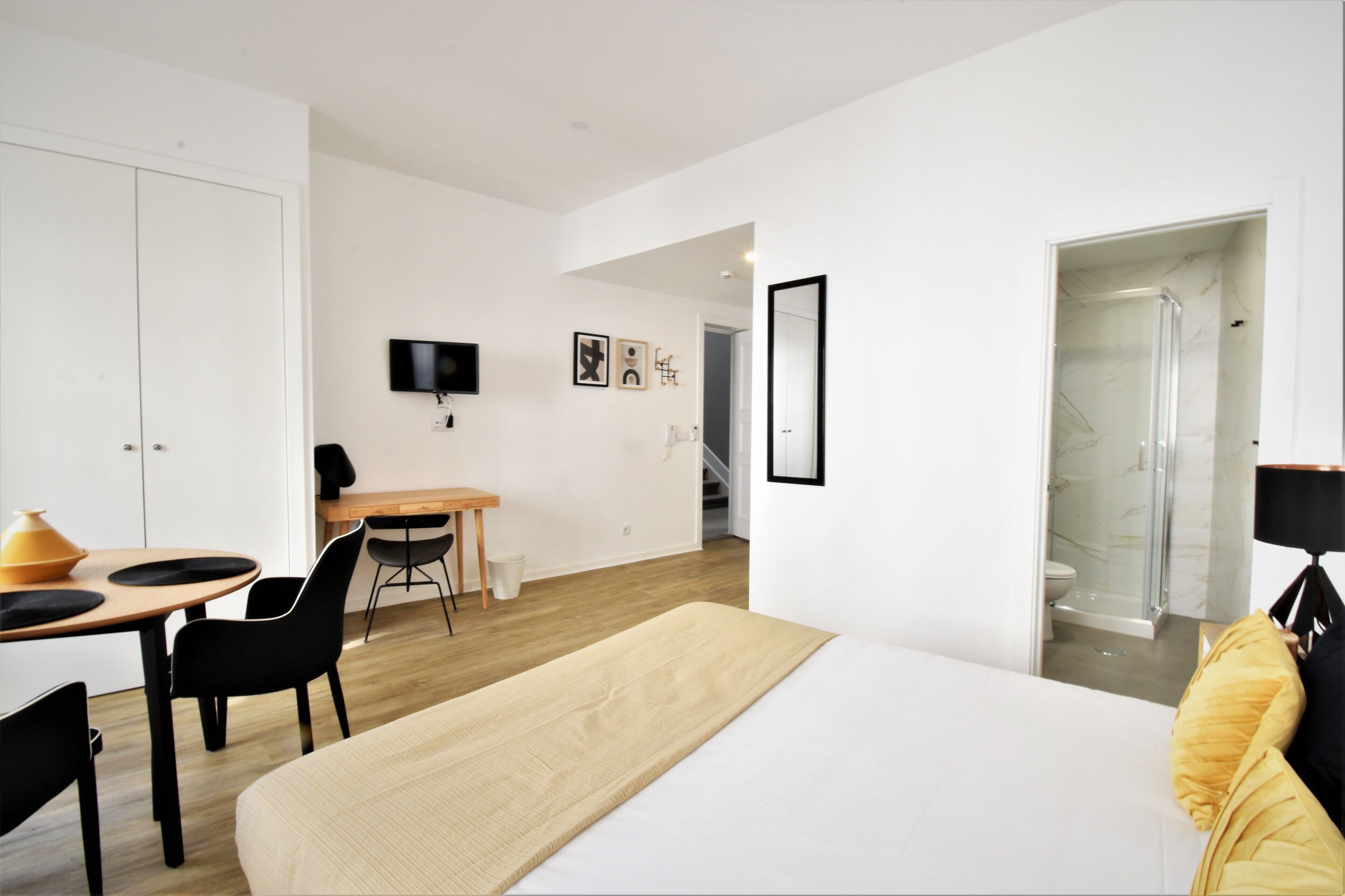 A modern hotel room with a large bed, a desk with chairs, a TV, and a shower area.