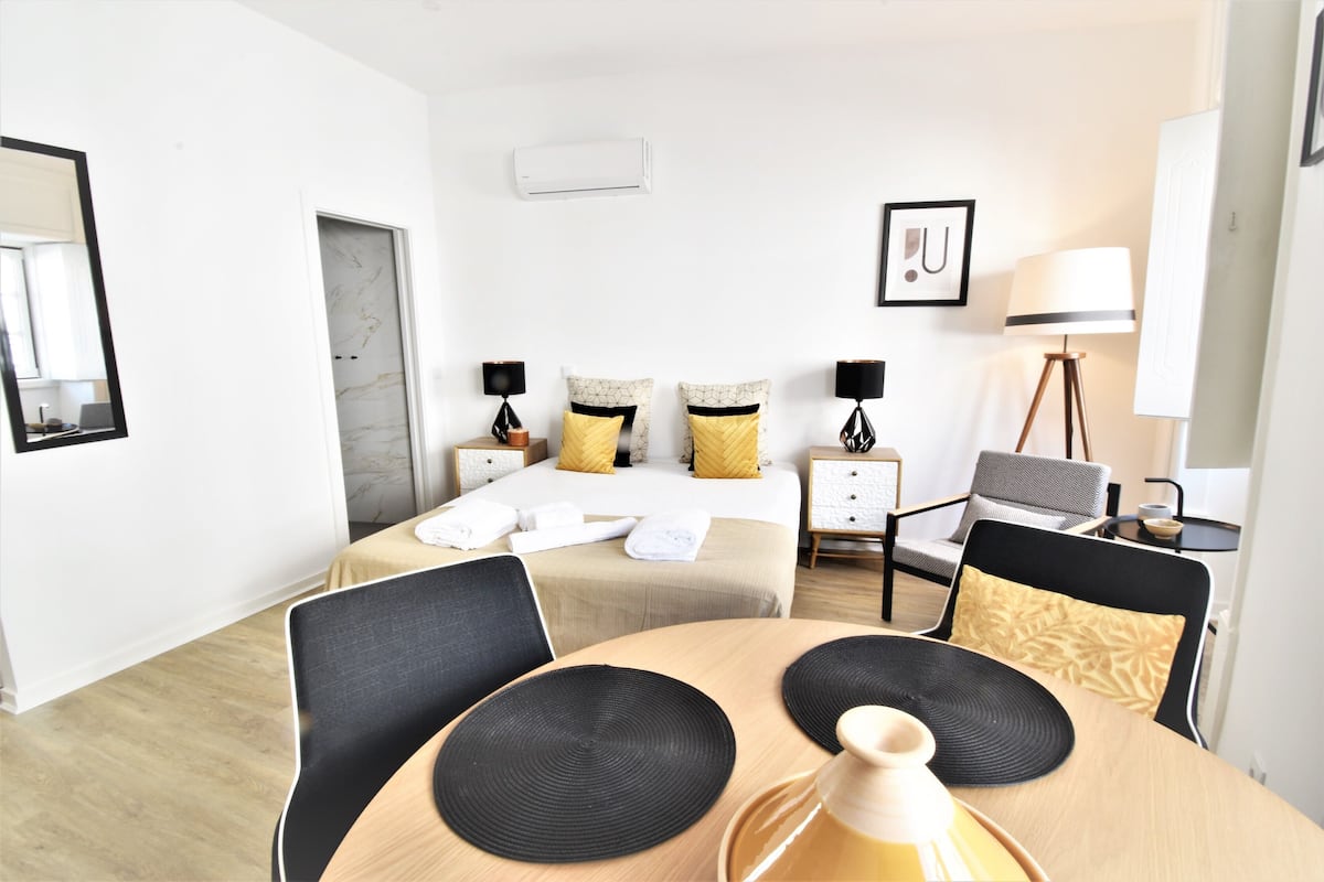 Quarto de hotel com cama, mesas de cabeceira, luminária, cadeira, mesa e espelho.