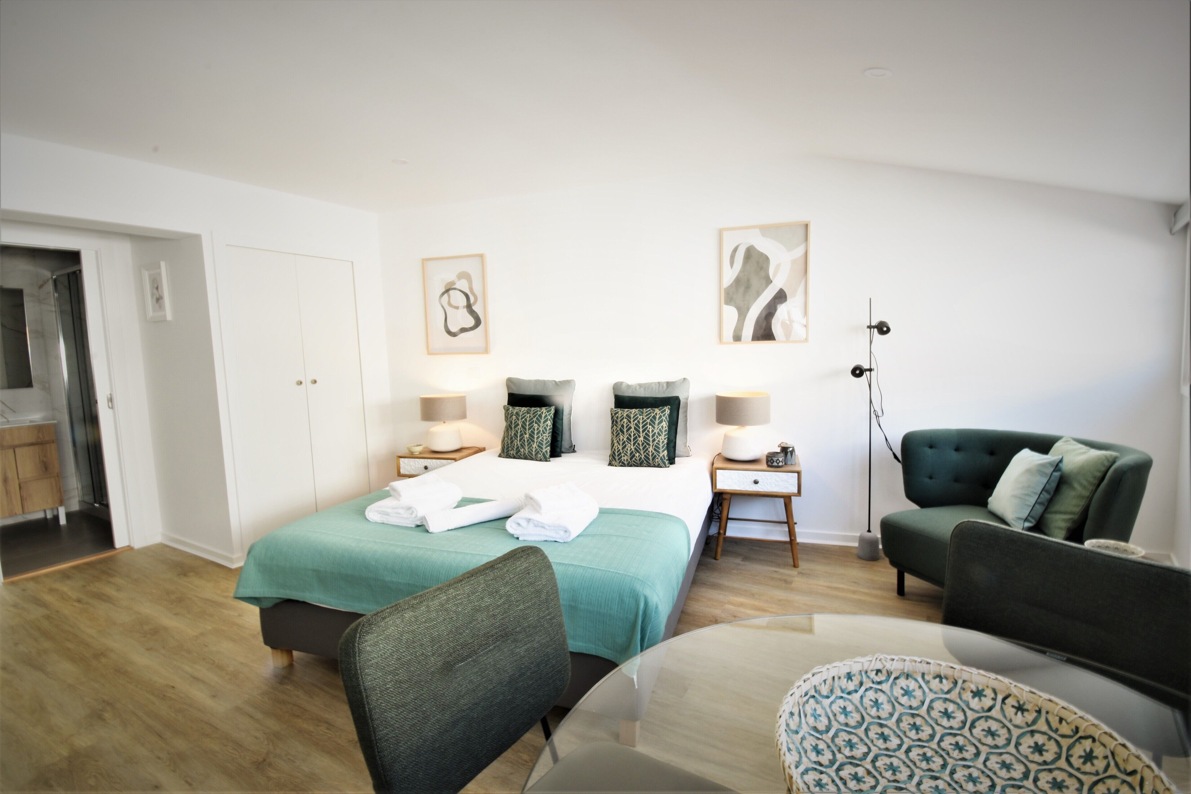 A hotel room with a bed, two bedside tables, a chair, a sofa, and a floor lamp.