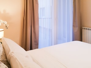 A hotel room with a bed, a nightstand, a lamp, and a window with curtains.