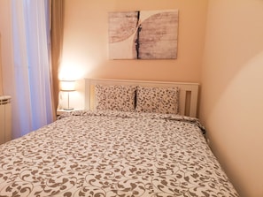 A neatly made bed with a patterned bedspread, a bedside lamp, and a wall-mounted artwork.