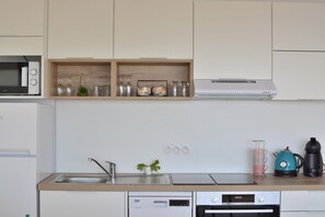 Une cuisine moderne équipée d’un four à micro-ondes, d’un four et d’une machine à café intégrés. On y trouve des étagères avec de la verrerie et une petite plante.