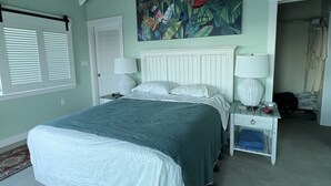 Een slaapkamer met een groot bed, een nachtkastje, een plafondventilator, een schilderij en een raam met blinds.