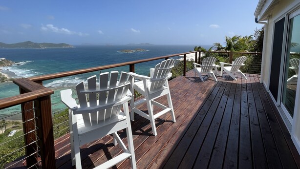 Een houten terras met witte Adirondack-stoelen met uitzicht op de kust.