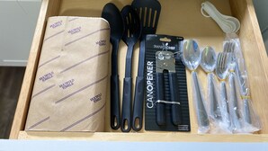 A drawer containing kitchen utensils including a can opener, spatulas, and a package of foldable towels. - Great Place to Relax! (Cleveland)
