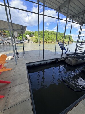 A dock with chairs, a pool, and a view of a lake with trees and buildings in the background.
