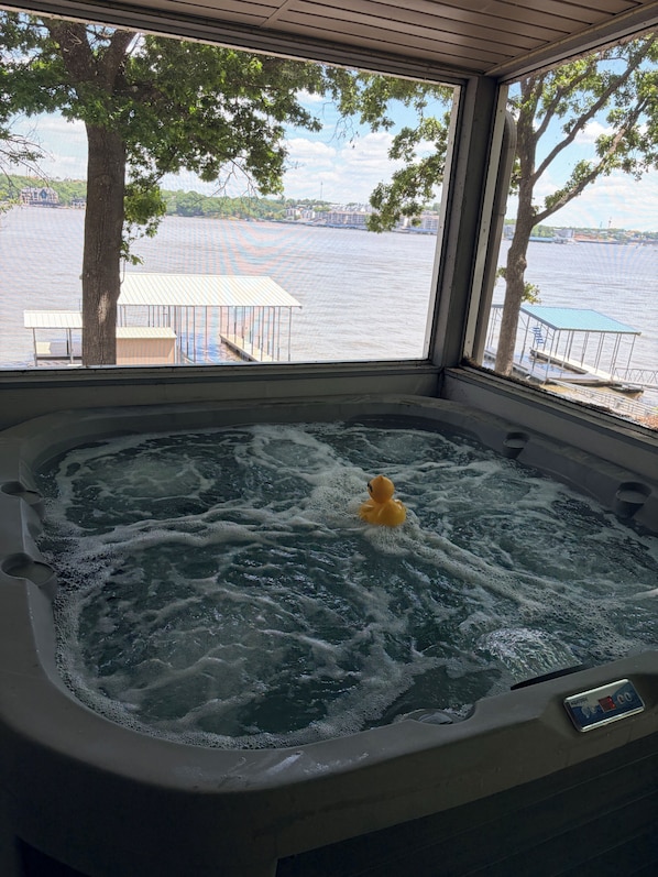 A hot tub with a duck, a view of a lake, and a dock with a covered seating area.