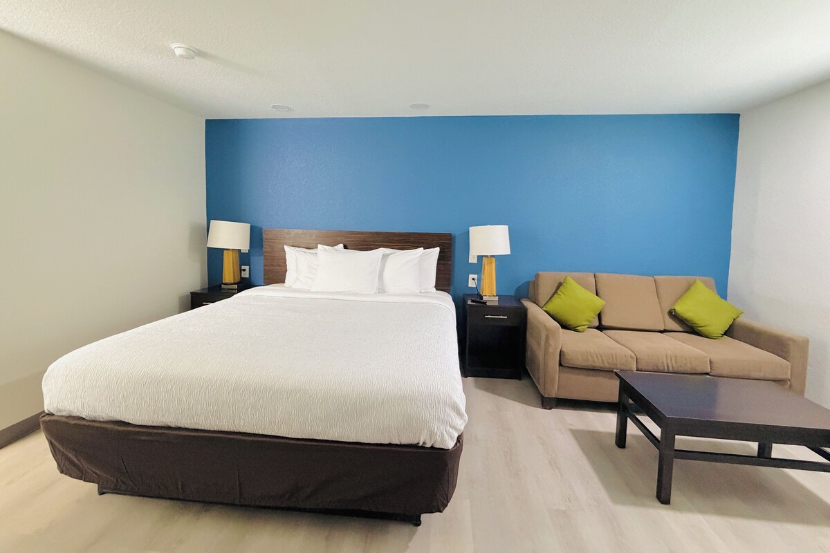 A hotel room with a large bed, a sofa, a coffee table, and two bedside tables with lamps.