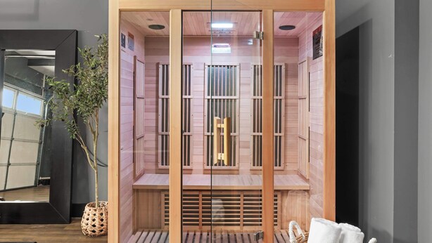 A sauna with wooden walls and a glass partition, a potted plant, and a towel on the floor.