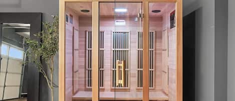 Una sauna con paredes de madera y una mampara de vidrio, una planta en maceta y una toalla en el suelo.
