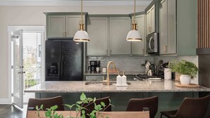 A kitchen with two pendant lights, a refrigerator, a coffee maker, and a sink.