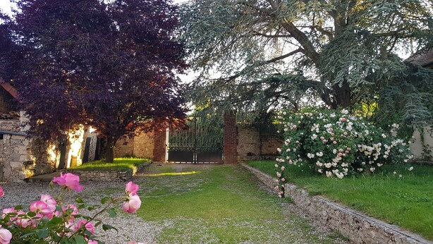 Um jardim com muro de pedra, portão de madeira e rosas em flor.