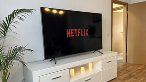 Un televisor de pantalla plana sobre un mueble blanco, con una planta al lado.