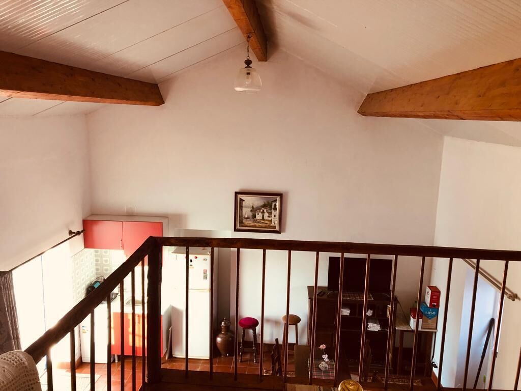 Une pièce avec un plafond en bois, un escalier doté d’une rampe, un coin cuisine avec un réfrigérateur et une table à manger avec des chaises.