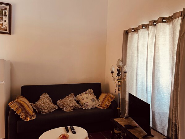 Un salon avec un canapé noir, une petite table ronde, un lampadaire et une fenêtre avec des rideaux.