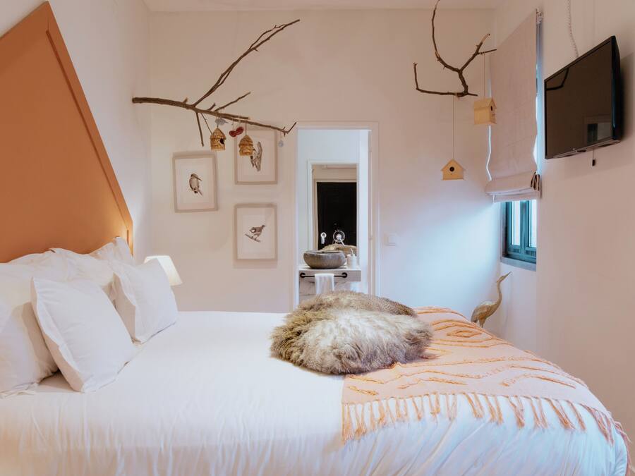 A bedroom with a bed, a window, a wall-mounted TV, and a door leading to another room.