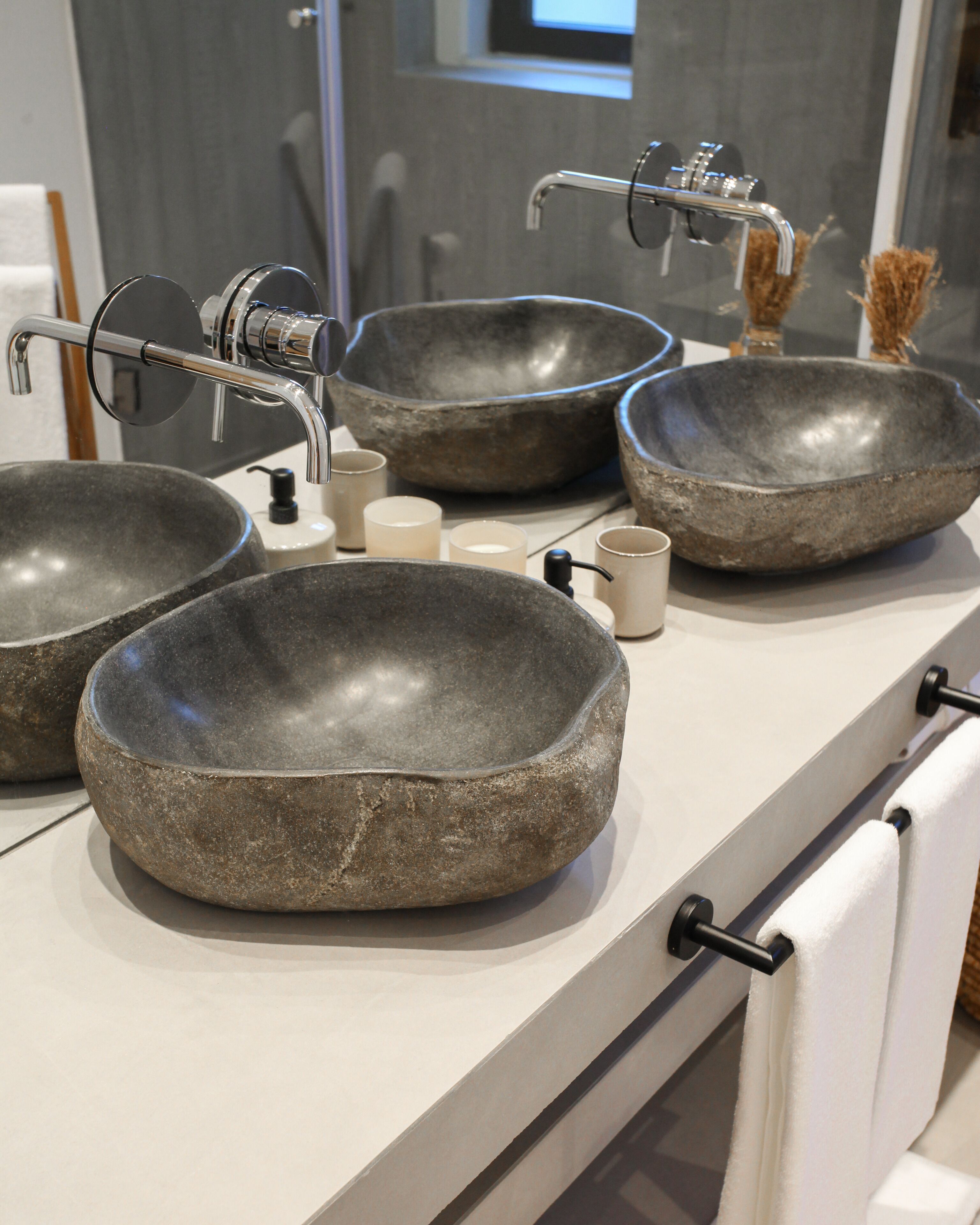 Een badkamer met drie grote stenen kommen als wasbakken, een moderne kraan en een witte handdoekhouder.