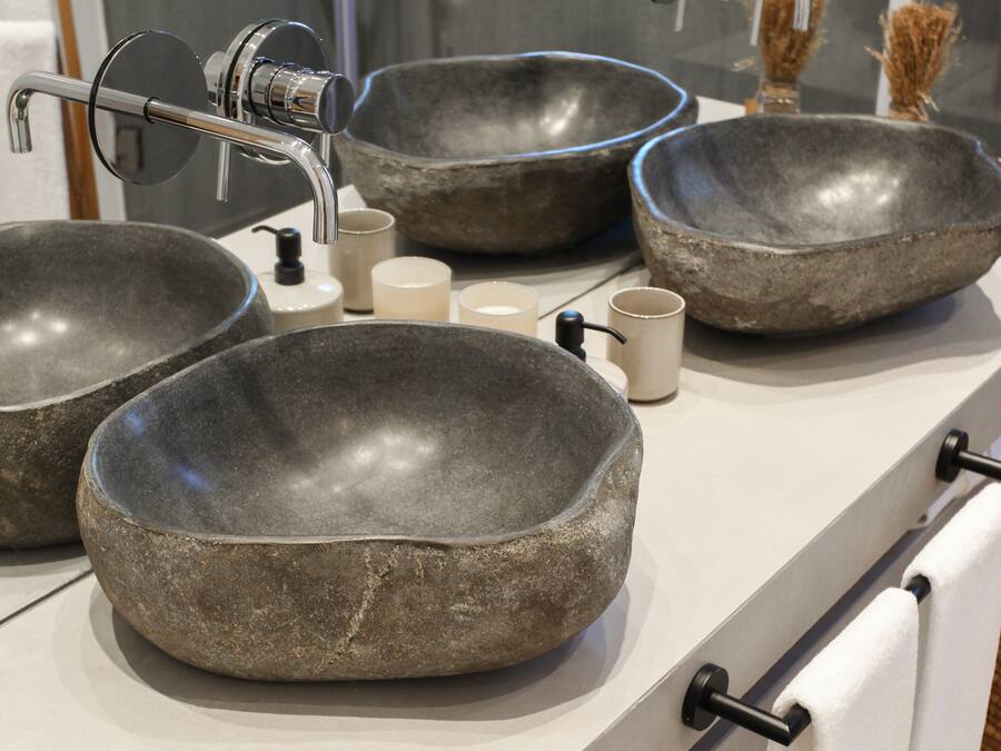 A bathroom with three large stone bowls as sinks, a modern faucet, and a white towel rack.