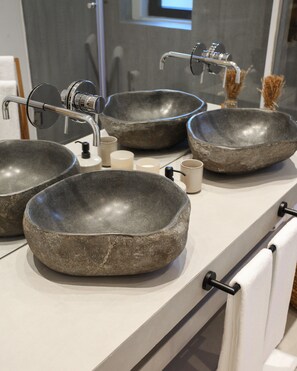 A bathroom with three large stone bowls as sinks, a modern faucet, and a white towel rack.