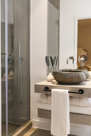 Un baño moderno con ducha de vidrio, lavabo de piedra y toallero.
