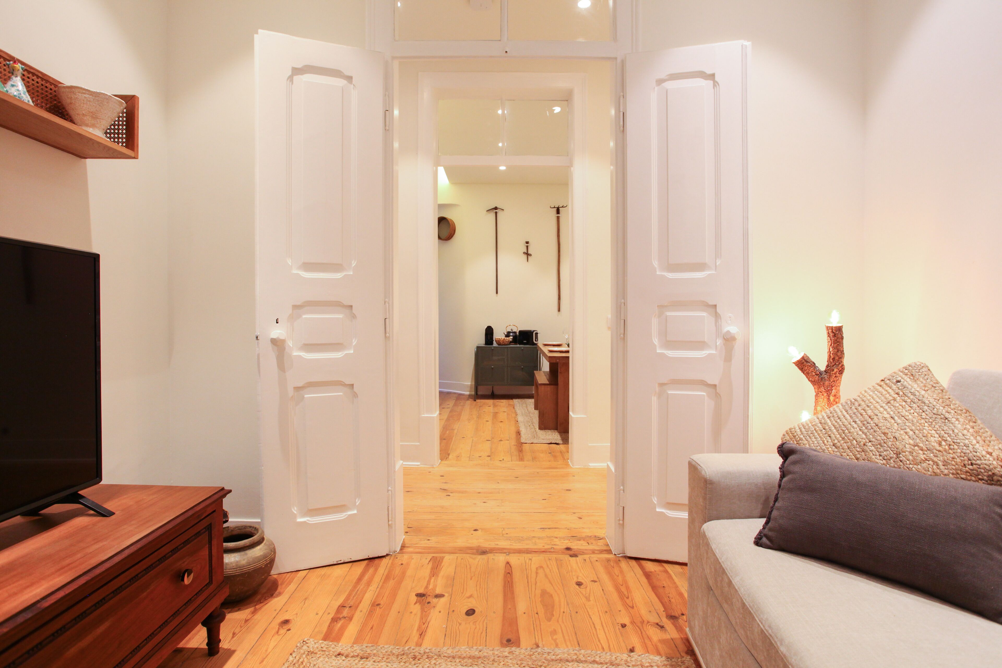 An open doorway leading to a living area with a television, a sofa, and a wooden floor.