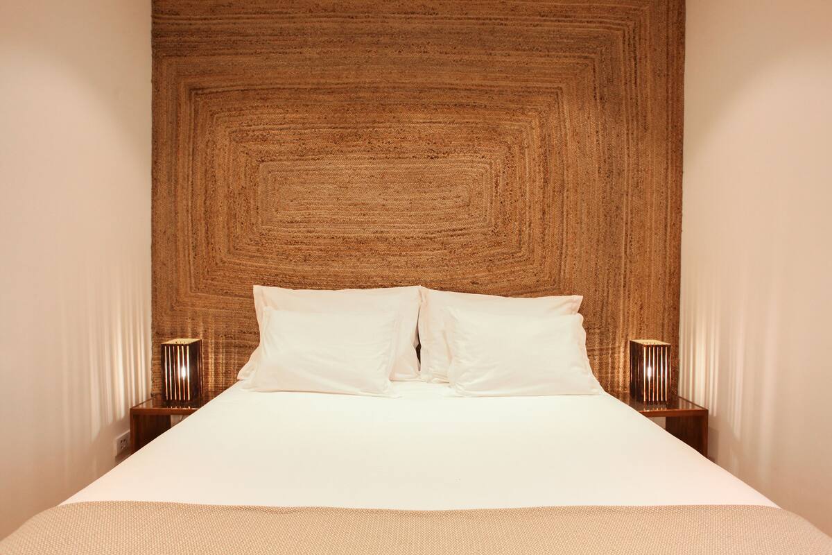 A neatly made bed with two pillows, a wooden headboard, and two bedside lamps on either side.