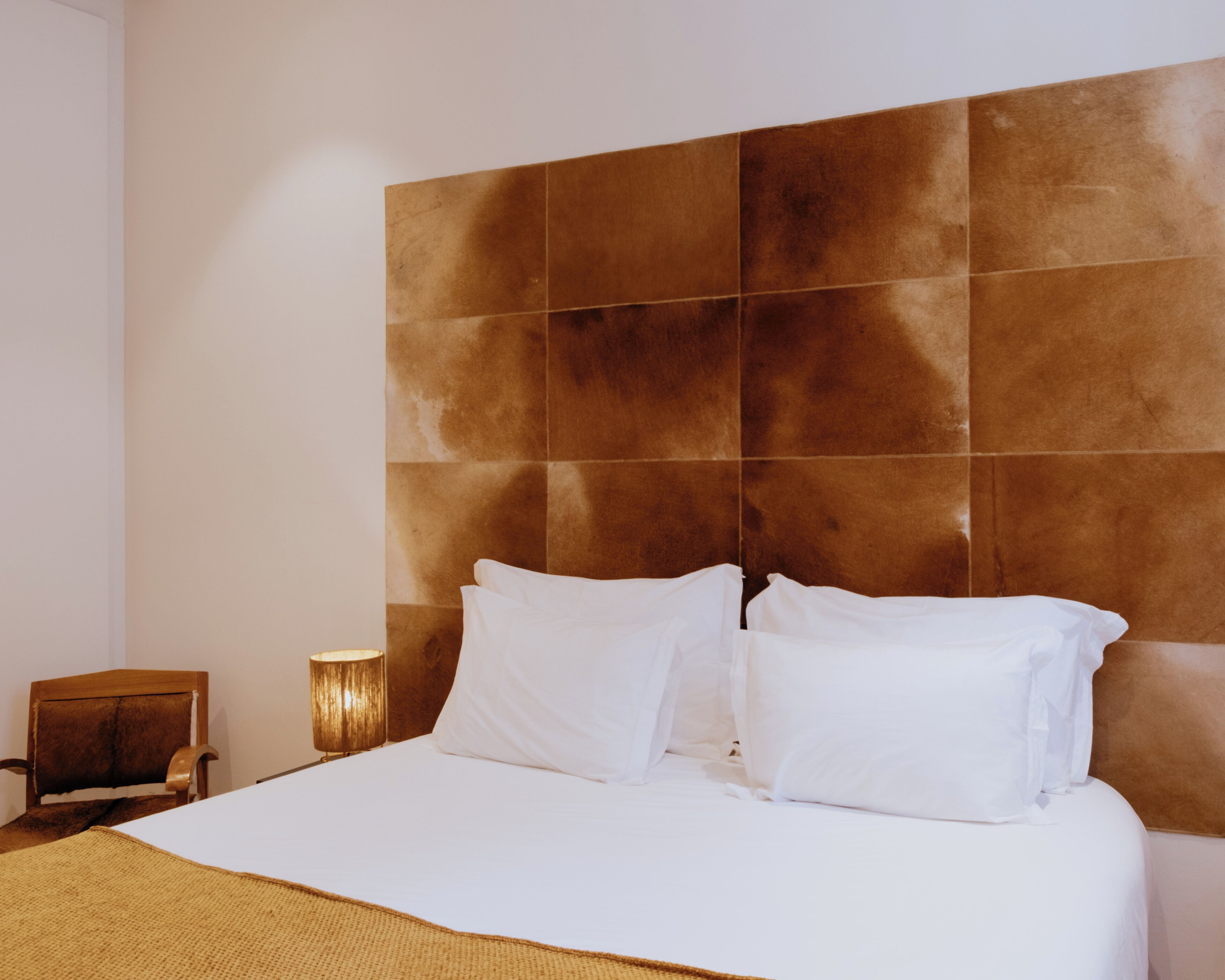 A hotel room with a large bed, a nightstand, and a wall-mounted headboard.